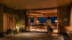 夜の海辺から温泉宿の明るいロビーへ戻る旅行者の後ろ姿