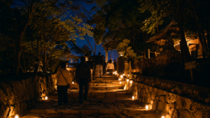 ろうそくの明かりが続く夜の寺院参道を静かに歩く人々