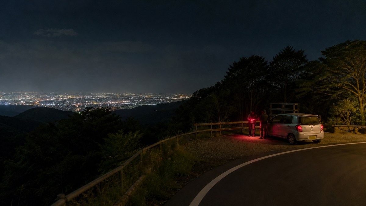 菜の花台を想起させる展望駐車スペースから秦野市街の夜景を見る旅行者のAI生成イメージ