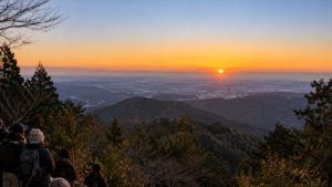 高尾山の東側展望から冬の朝日を待つ登山客と関東平野を描いた実写風AI生成画像